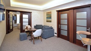 A modern hotel room with a dining area, a sofa, a small table, and a chair. There are wooden doors with frosted glass panels and a painting on the wall. - North Gate Avenue (Yerevan)