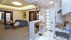 A modern kitchen with a marble countertop, a built-in sink, and a bar area with stools. There is a dining area with a table and chairs, and a living room with a sofa and a coffee table. - North Gate Avenue (Yerevan)