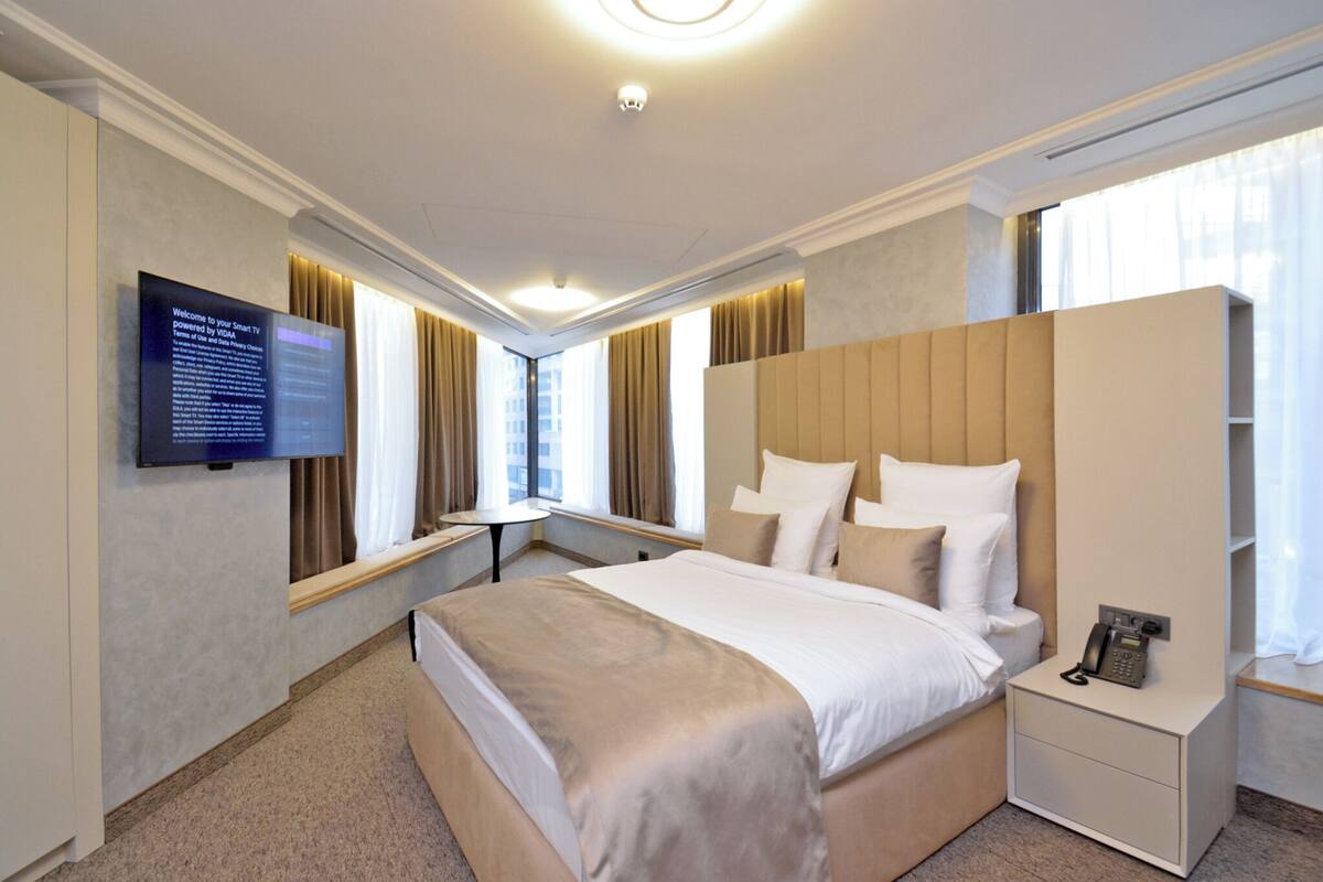 A modern hotel room with a large bed, bedside tables, a TV, and a wardrobe.