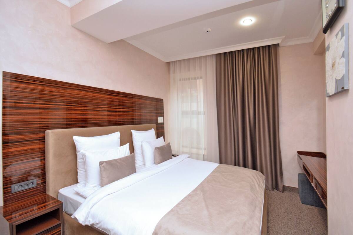 A hotel room with a large bed, a wooden headboard, a bedside table, and a desk with a chair.
