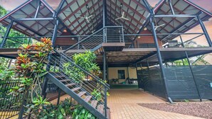 A modern building with a triangular roof structure, multiple levels, and outdoor seating areas. - Zenlux Tropical Retreat Pool BBQ Golf Course (Darwin)