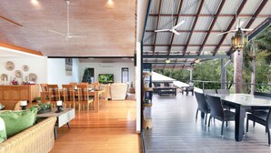 A spacious indoor area with a dining area, a seating area with a sofa, and a covered outdoor deck with tables and chairs. - Zenlux Tropical Retreat Pool BBQ Golf Course (Darwin)