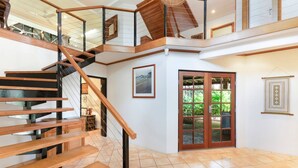 A spacious interior with a wooden staircase leading to a balcony, a large sliding glass door, and a framed picture on the wall. - Zenlux Tropical Retreat Pool BBQ Golf Course (Darwin)