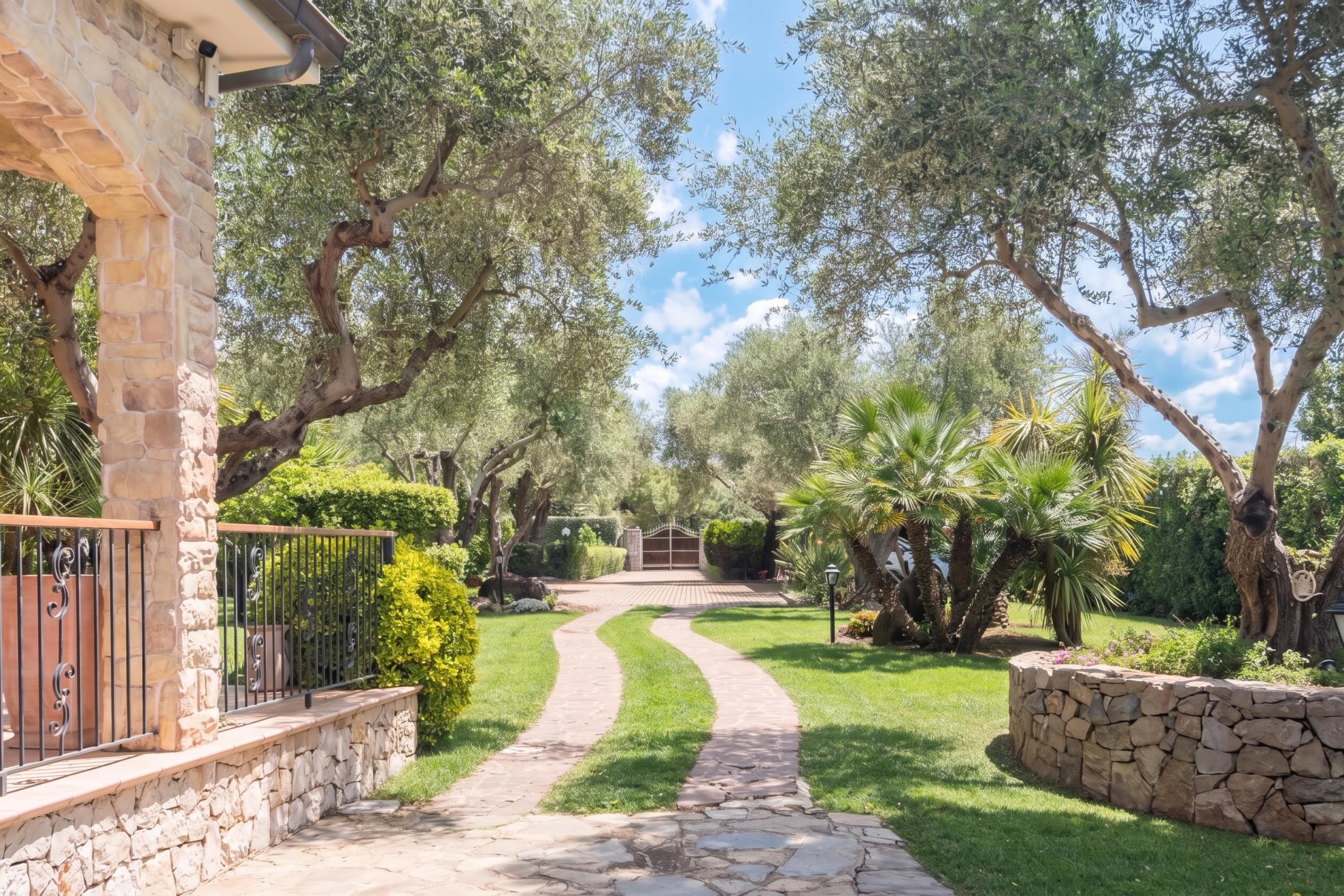 A stone pathway leading to a gated entrance, surrounded by lush greenery and trees.
