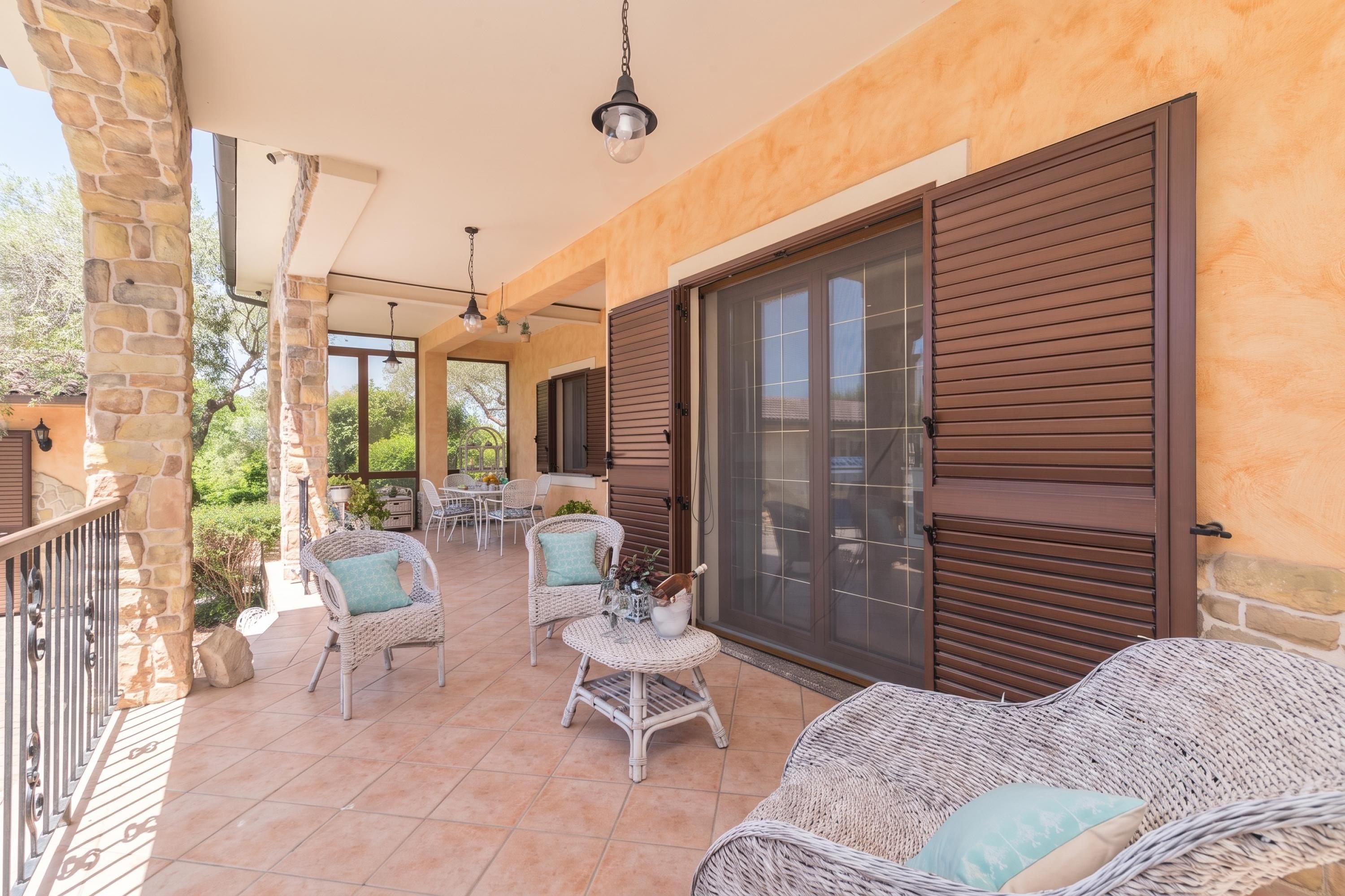 Une terrasse extérieure couverte, aménagée avec des meubles en osier, un pilier en pierre et une porte-fenêtre coulissante.