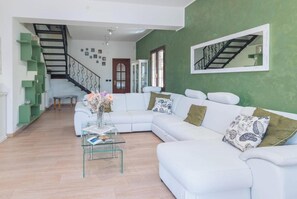 A living room with a white sectional sofa, a glass coffee table, a staircase, and a green accent wall. - Dimora Patrizia (Alghero)
