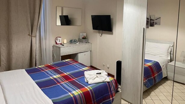 A hotel room with two beds, a desk, a television, and a mirror.