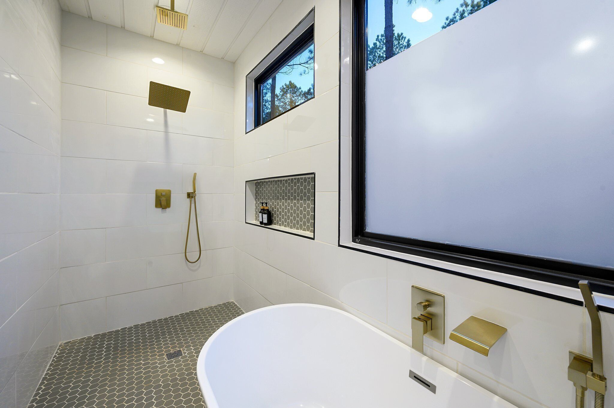 Un bagno moderno con una vasca da bagno freestanding, una doccia con soffione a mano e una finestra che offre luce naturale.