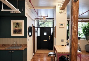 Un couloir étroit mène à une porte noire ornée d’un miroir et d’un tableau encadré accroché au mur.