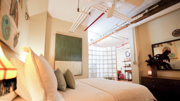 A bedroom with a large bed, a dresser, and a mirror. There is a window with a view of the outside. - Bright Artist Loft in Williamsburg Brooklyn (Brooklyn)