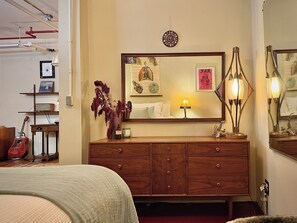 Ein Schlafzimmer mit einem Holzkoffer, einem Bett, einer Gitarre und einem Spiegel mit Kunstwerken.
