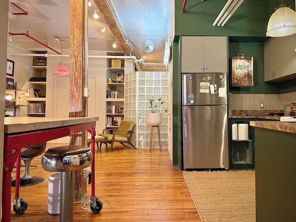 A modern kitchen with a stainless steel refrigerator, wooden flooring, and a green accent wall.