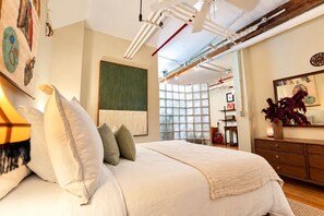 Une chambre avec un grand lit, un tableau abstrait aux tons verts, une commode en bois et un miroir.