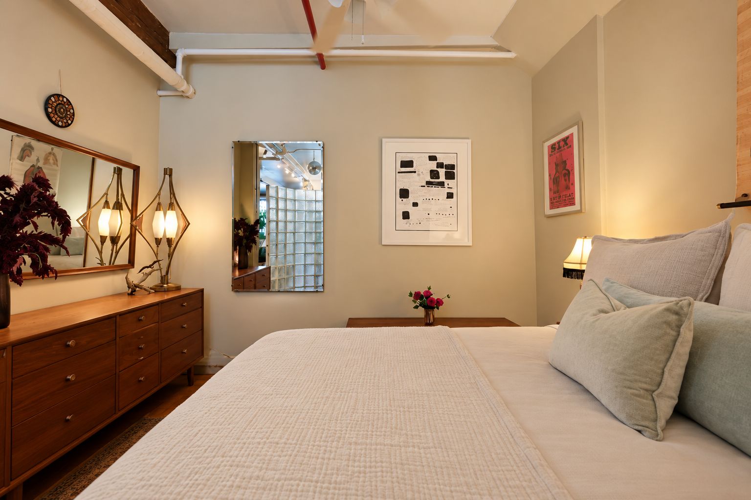 Ein Schlafzimmer mit einem großen Bett, einer Holzkommode, einem Spiegel und Wandbildern.