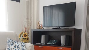 A living room with a sofa, a table, a television on a stand, and a radiator. - At 900 mt. Spa, 1 km the sea, Oltremare/Aquafan, 10 min. walk, 5 min. by bike (Riccione)