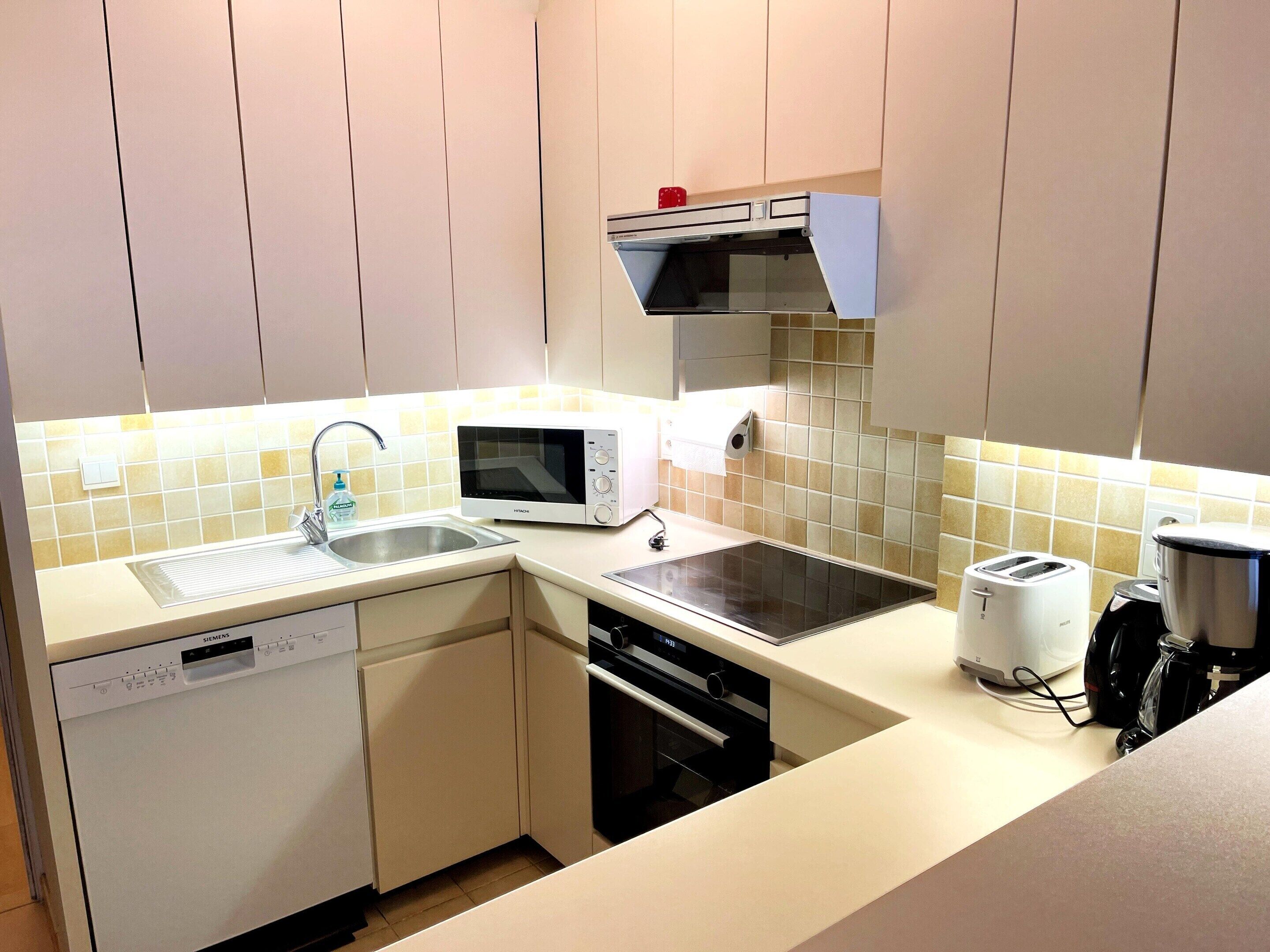 A compact kitchen with a dishwasher, microwave, toaster, and a sink.