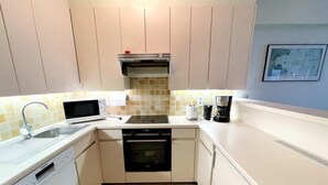 A compact kitchen with white cabinets, a stainless steel range hood, a microwave, a toaster, and a coffee maker.