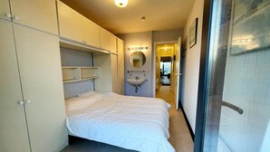 A compact bedroom with a bed, built-in wardrobe, and a bathroom with a sink and mirror.