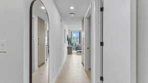 A modern hallway with white walls, a tiled floor, and a view of a cityscape through an open door. - Luxury 1BR | Rooftop Pool | Miami Worldcenter (Miami)