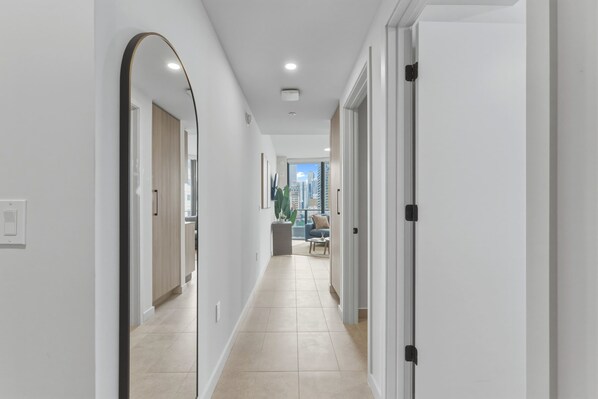 A modern hallway with white walls, a tiled floor, and a view of a cityscape through an open door. - Luxury 1BR | Rooftop Pool | Miami Worldcenter (Miami)