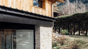 A modern wooden house with a stone foundation, large glass windows, and a view of snow-capped mountains. - Chalet aux ours with Aiguille du Midi view, ideal for families (7mn from the center) (Les Houches)