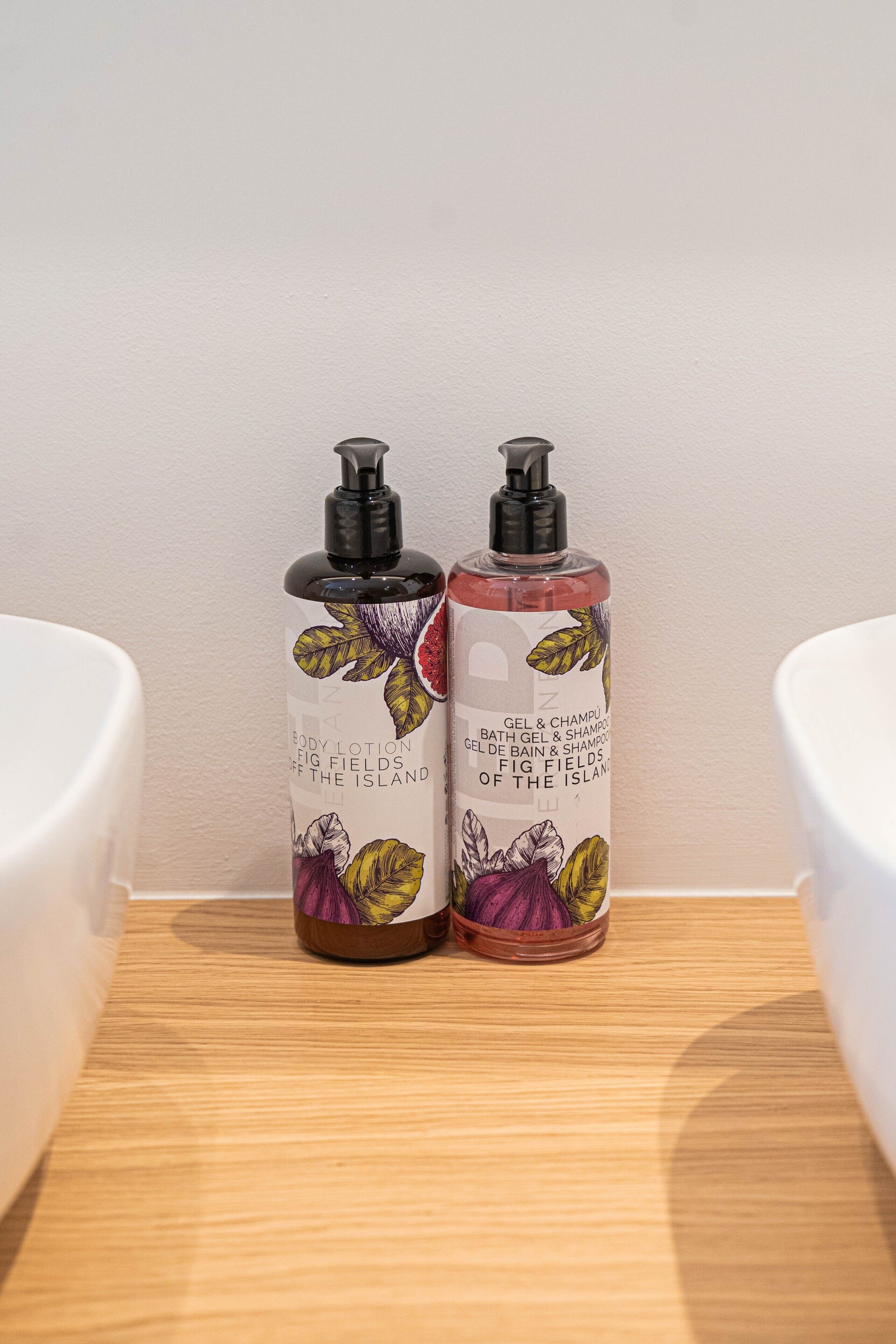 Two bottles of body lotion and shampoo on a wooden surface in a bathroom.