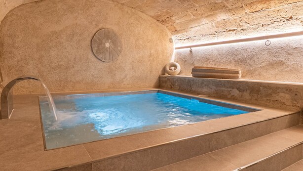 Piscina interior com paredes de pedra, superfície de água cristalina, elemento decorativo em formato circular e um banco embutido.