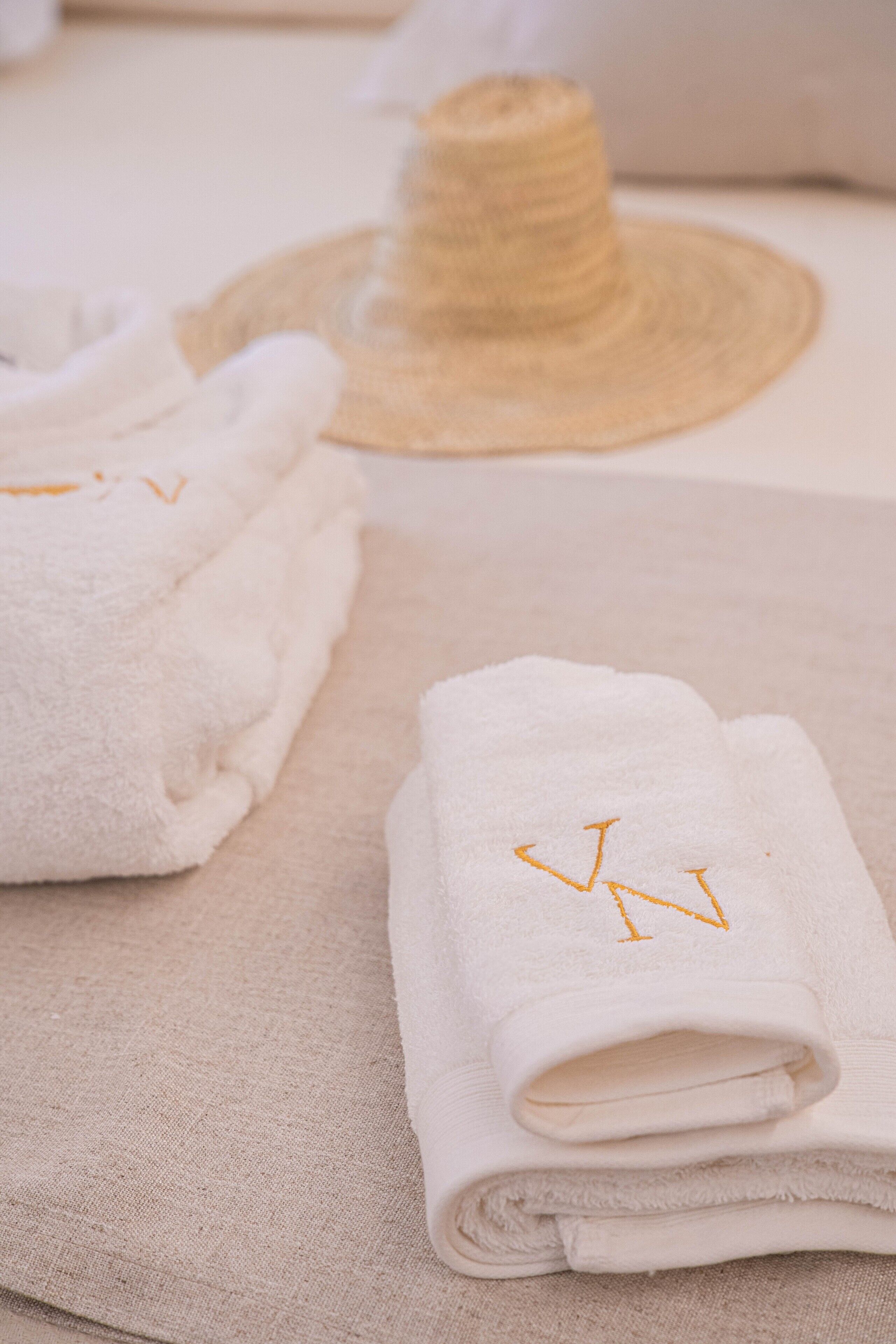Neatly folded white towels with embroidered initials on a textured surface.