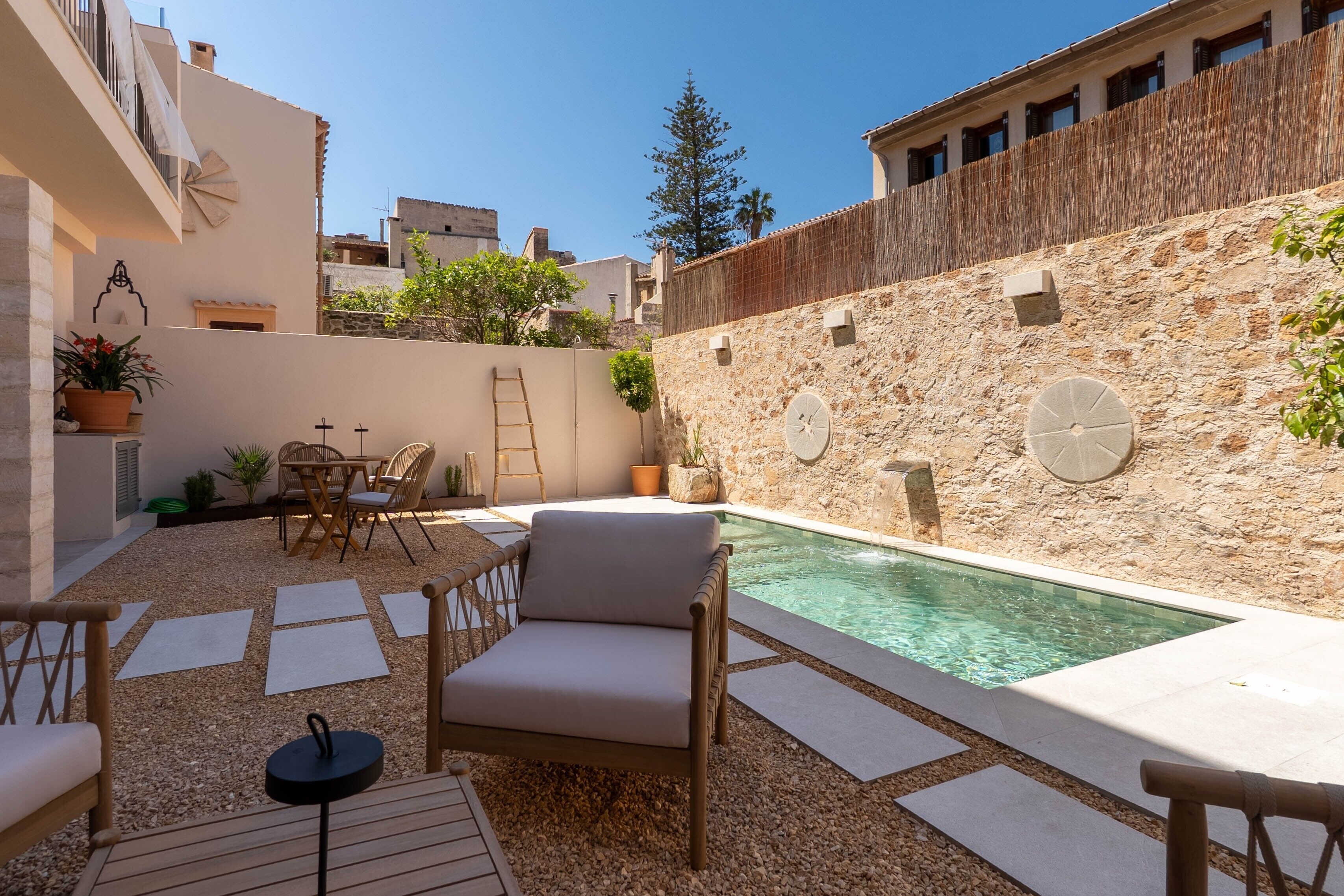 A courtyard with a swimming pool, outdoor seating, and a stone wall.