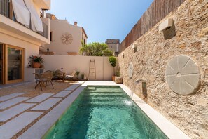 A swimming pool with a stone wall, a wooden deck, and outdoor furniture. - Room '201 - Junior Suite Con Balcón' with Sea View, Wi-Fi and Air Conditioning (Capdepera)