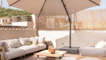 An outdoor seating area with a large umbrella, cushioned sofas, a wooden table, and decorative bottles.