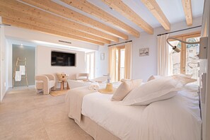 A bedroom with a bed, a TV, a window, and a bathroom with a bathtub and a chair. - Room '201 - Junior Suite Con Balcón' with Sea View, Wi-Fi and Air Conditioning (Capdepera)