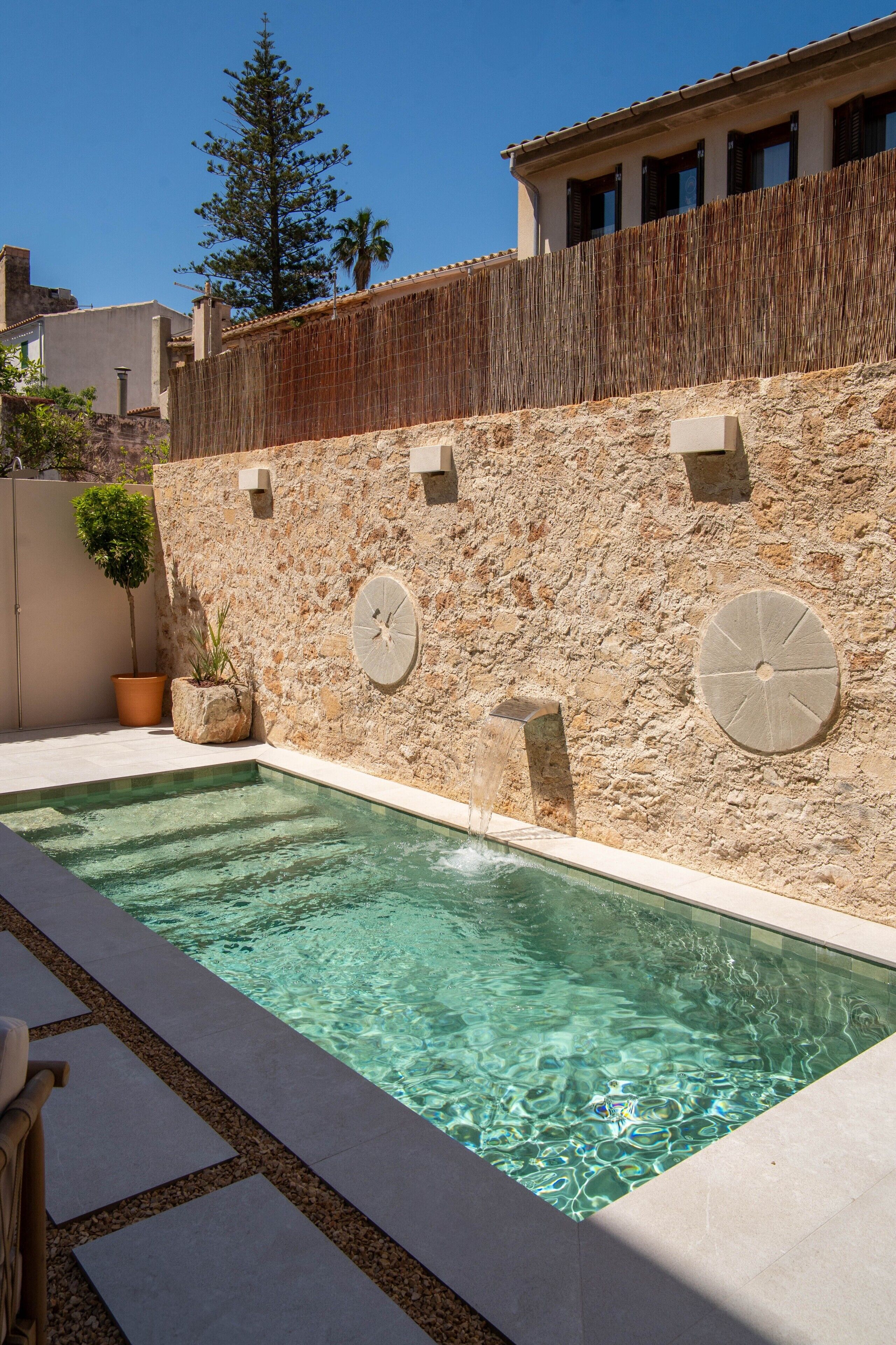A swimming pool with stone walls, a wooden fence, and potted plants.
