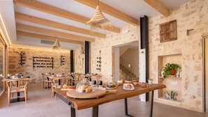 Un interior rústico con paredes de piedra vista, vigas de madera y una larga mesa de comedor con comida y bebidas.