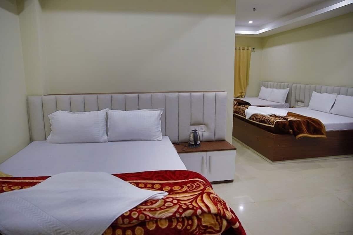 Een hotelkamer met een groot bed, een kleiner bed en een slaapbank. Er is een nachtkastje met een lamp en een stopcontact.