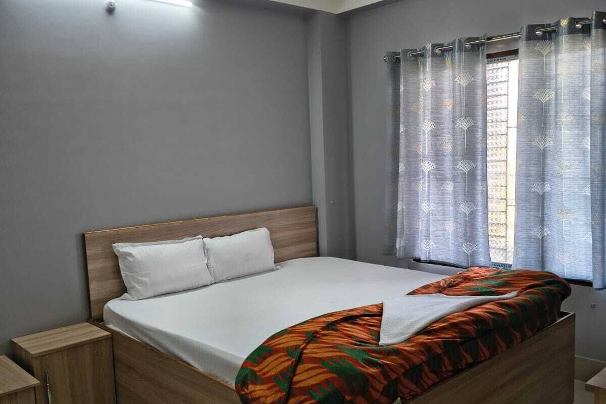 Een slaapkamer met een houten bed, nachtkastje, plafondventilator en een raam met gordijnen.