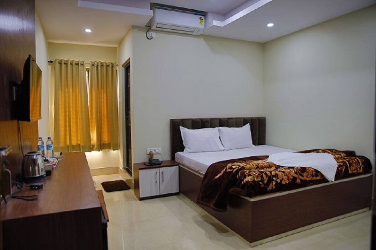 Een hotelkamer met een bed, bureau, televisie, kast en een airconditioning.