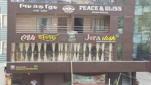 Un immeuble arborant plusieurs enseignes, notamment « Peace & Bliss Guest House » et « Jora Bliss Authentic Bengali Multi Cuisine ».