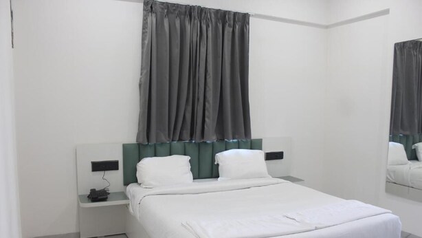 A modern hotel room with a large bed, a bedside table, and a mirror. - Zenora Stays (Pune)
