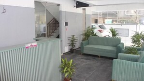 A reception area with a green sofa, potted plants, and a reception desk. - Zenora Stays (Pune)