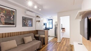Ein modernes Wohnzimmer mit einer Couch, einer Küchenzeile mit Kühlschrank und Spüle sowie einem Essbereich mit Hockstühlen.