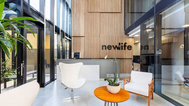 Ein moderner Empfangsbereich mit einem 'newlife'-Schild, zwei weißen Stühlen, einem Holztisch und einem Blumentopf.