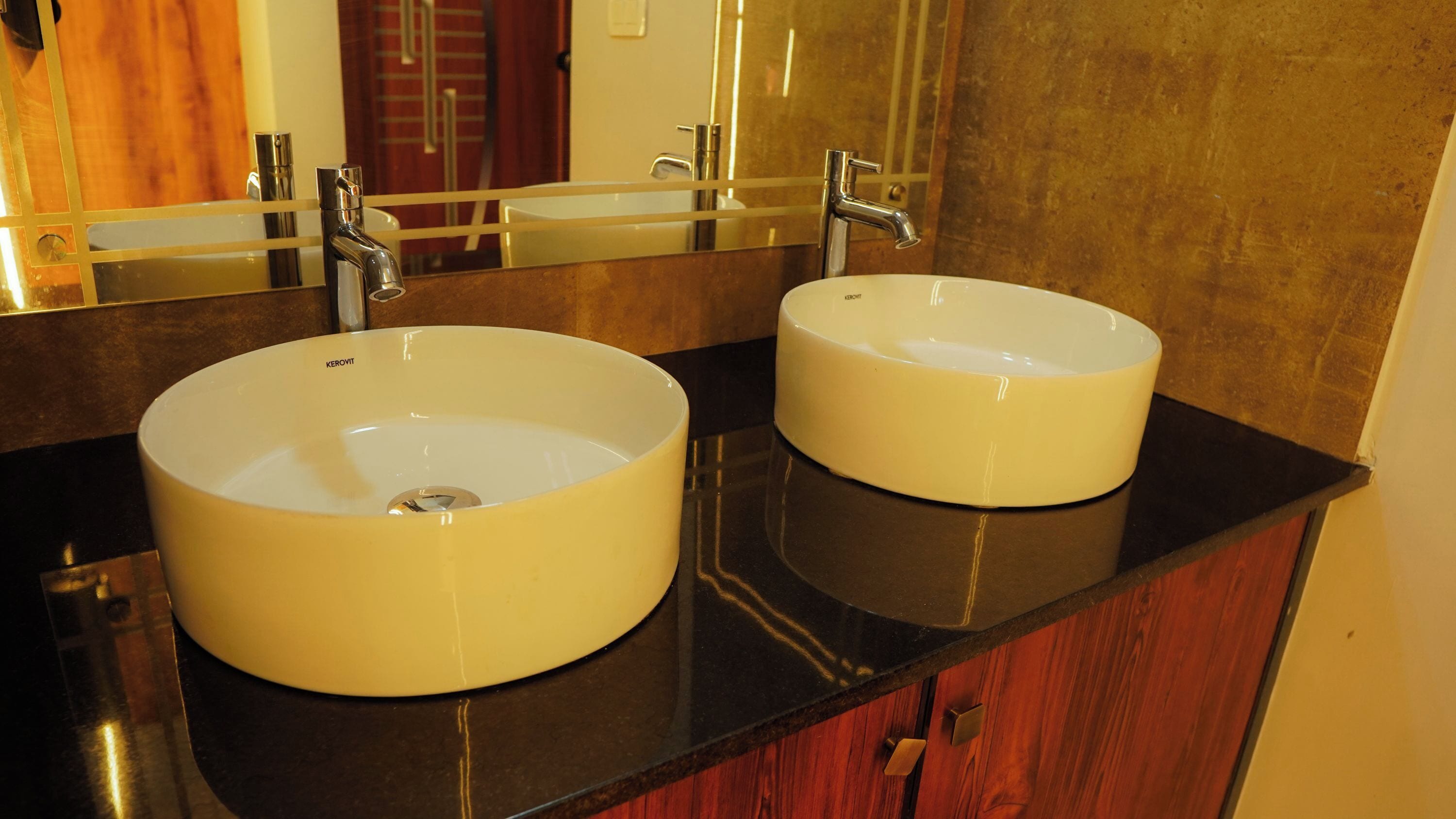 Two white sinks with chrome faucets on a black countertop, above a wooden vanity with a mirror.