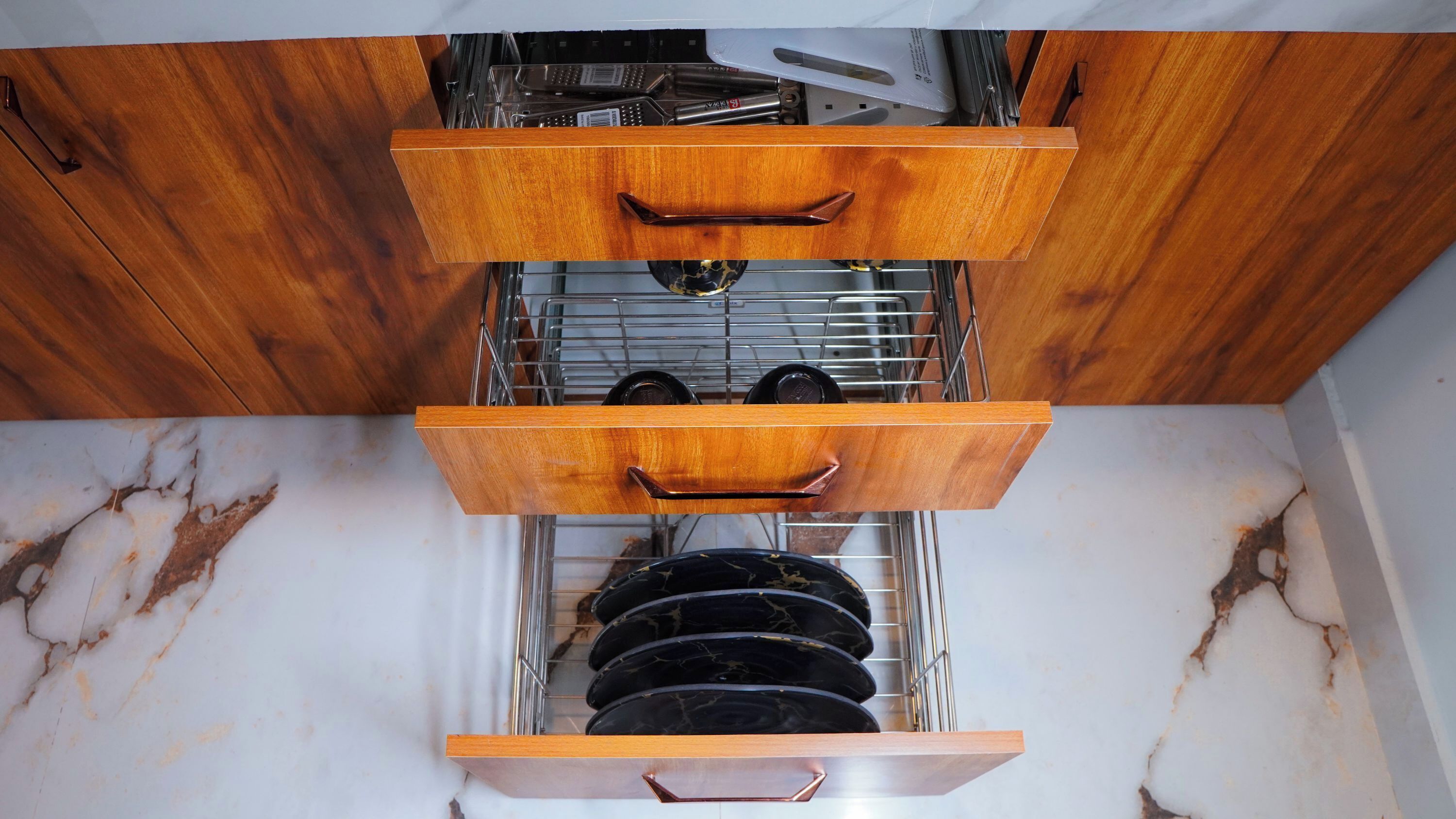 Una cocina con armarios de madera, encimera de mármol y escurreplatos con platos.