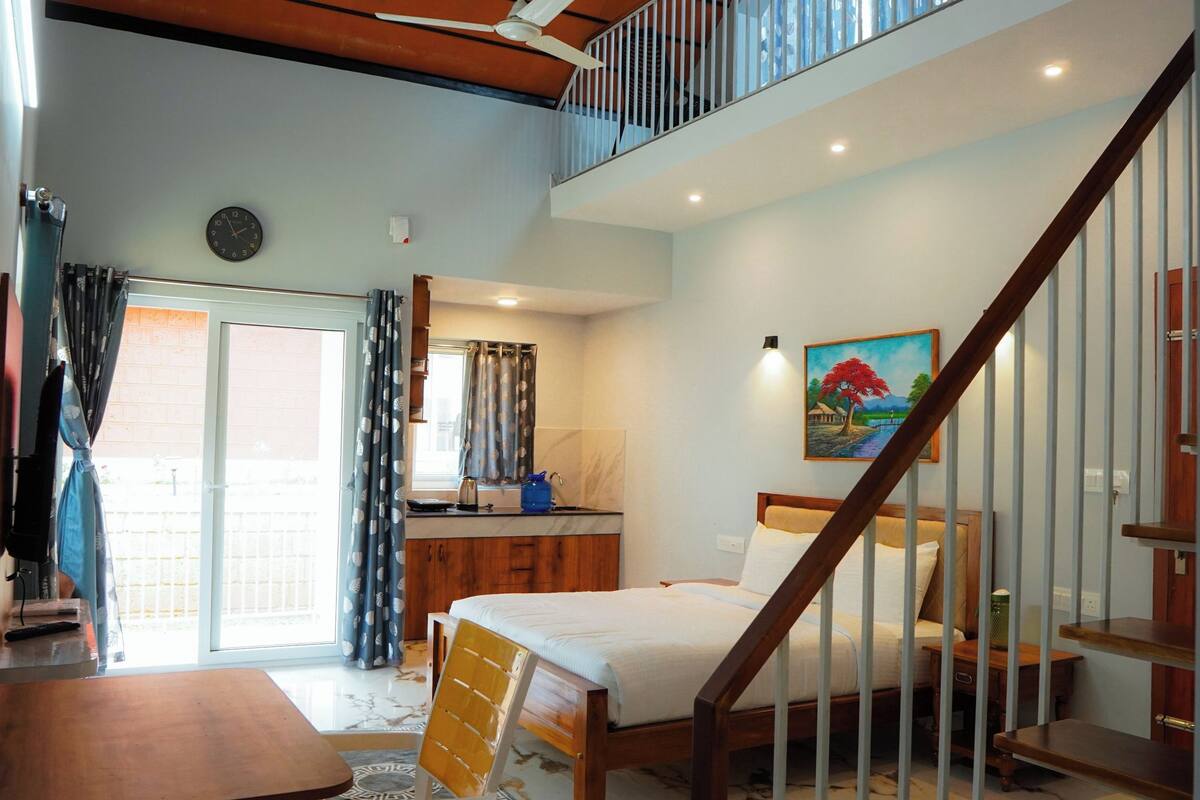 A bedroom with a bed, a desk, a chair, a window with curtains, a painting, a staircase, and a clock on the wall.