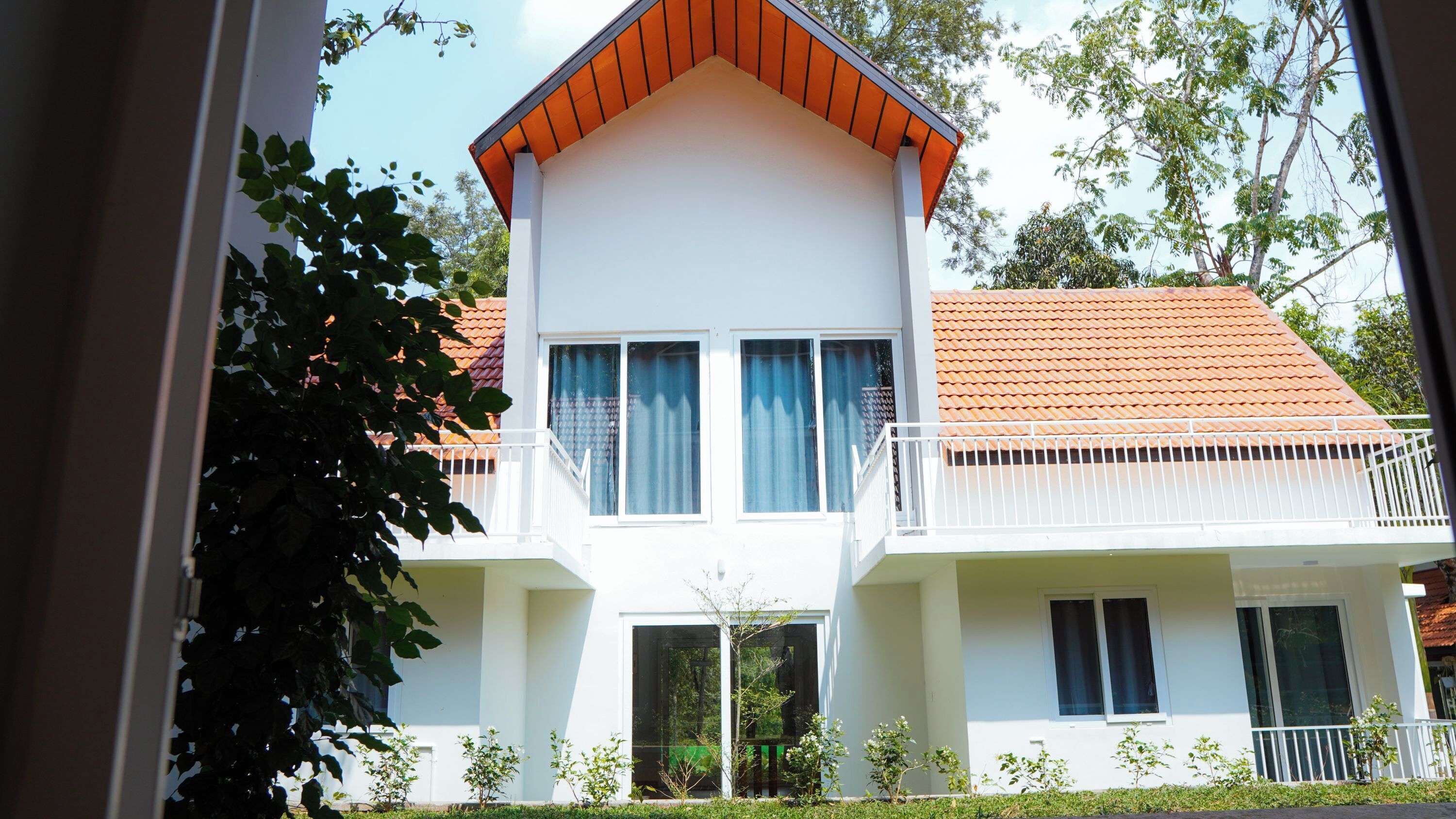 A two-story building with a white facade, a red-tiled roof, and a balcony with white railings.