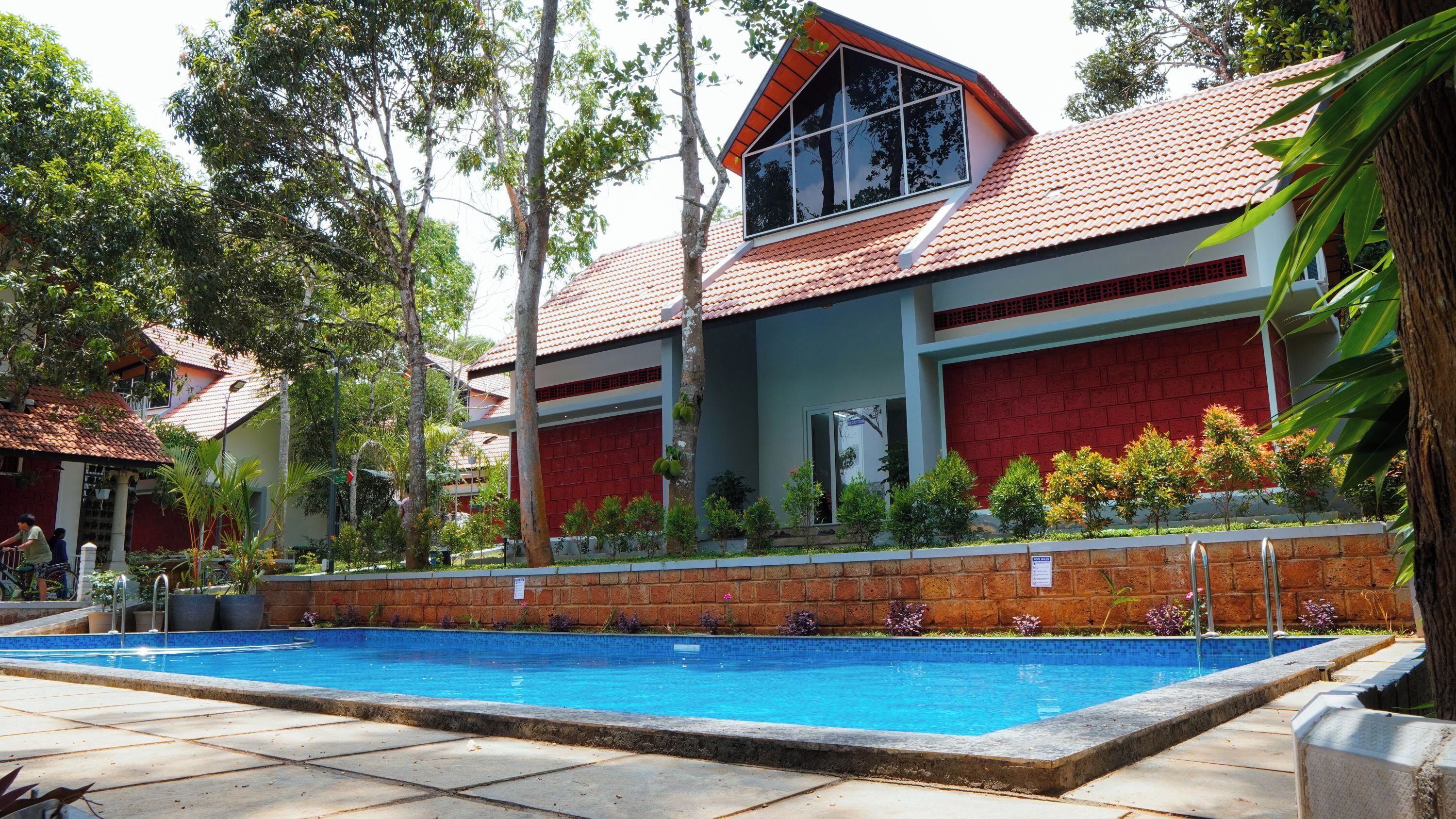 A swimming pool with a tiled deck, surrounded by a brick wall and greenery.