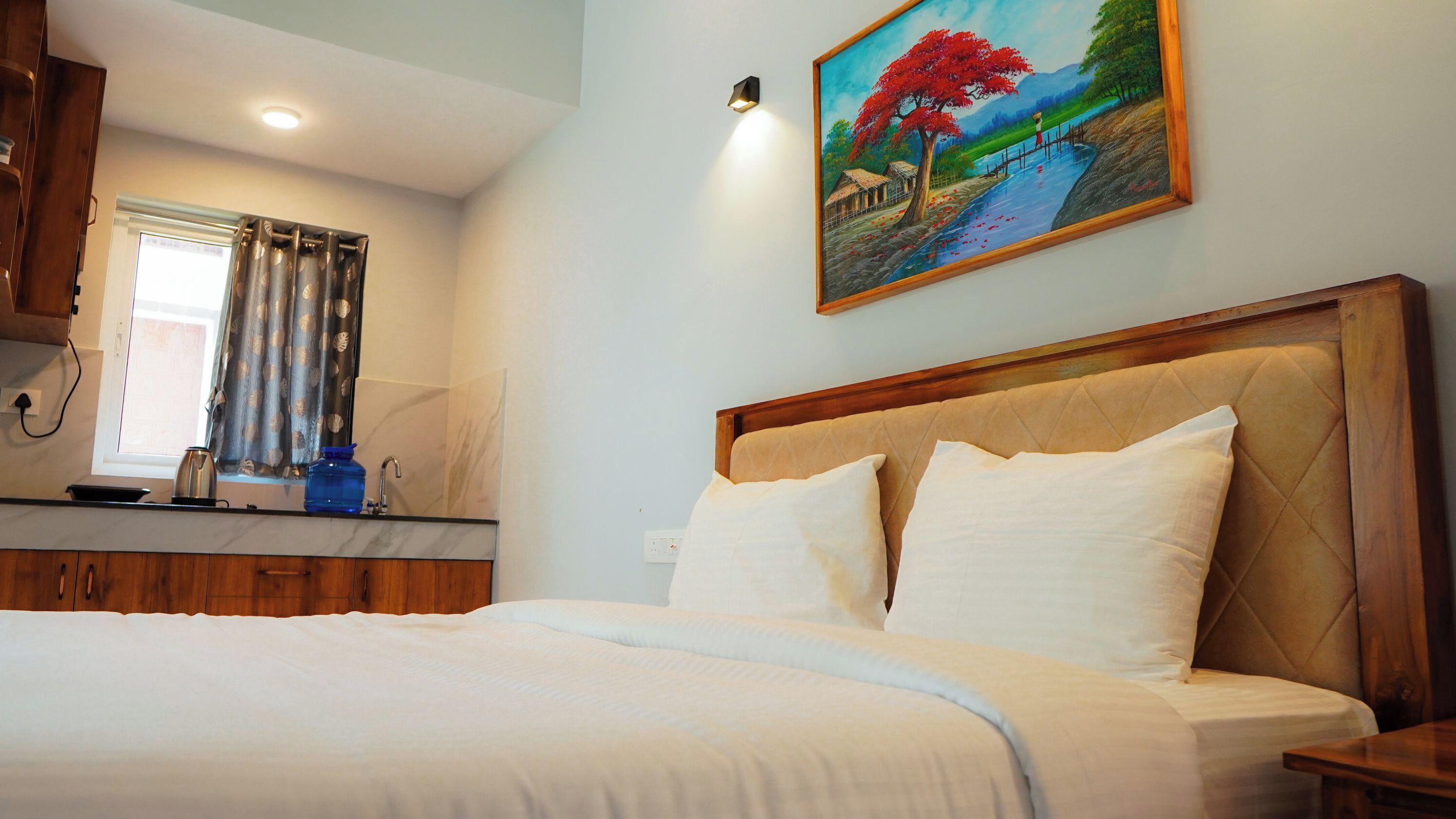 A bedroom with a bed, a painting of a landscape, a window with curtains, and a sink.