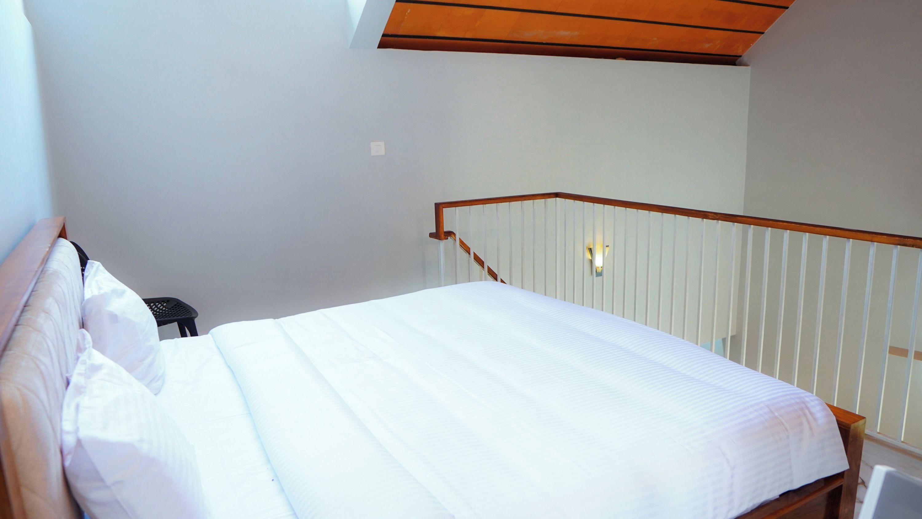 Une chambre à coucher comprenant un lit, une table de chevet, une lampe fixée au mur et un plafond en bois.
