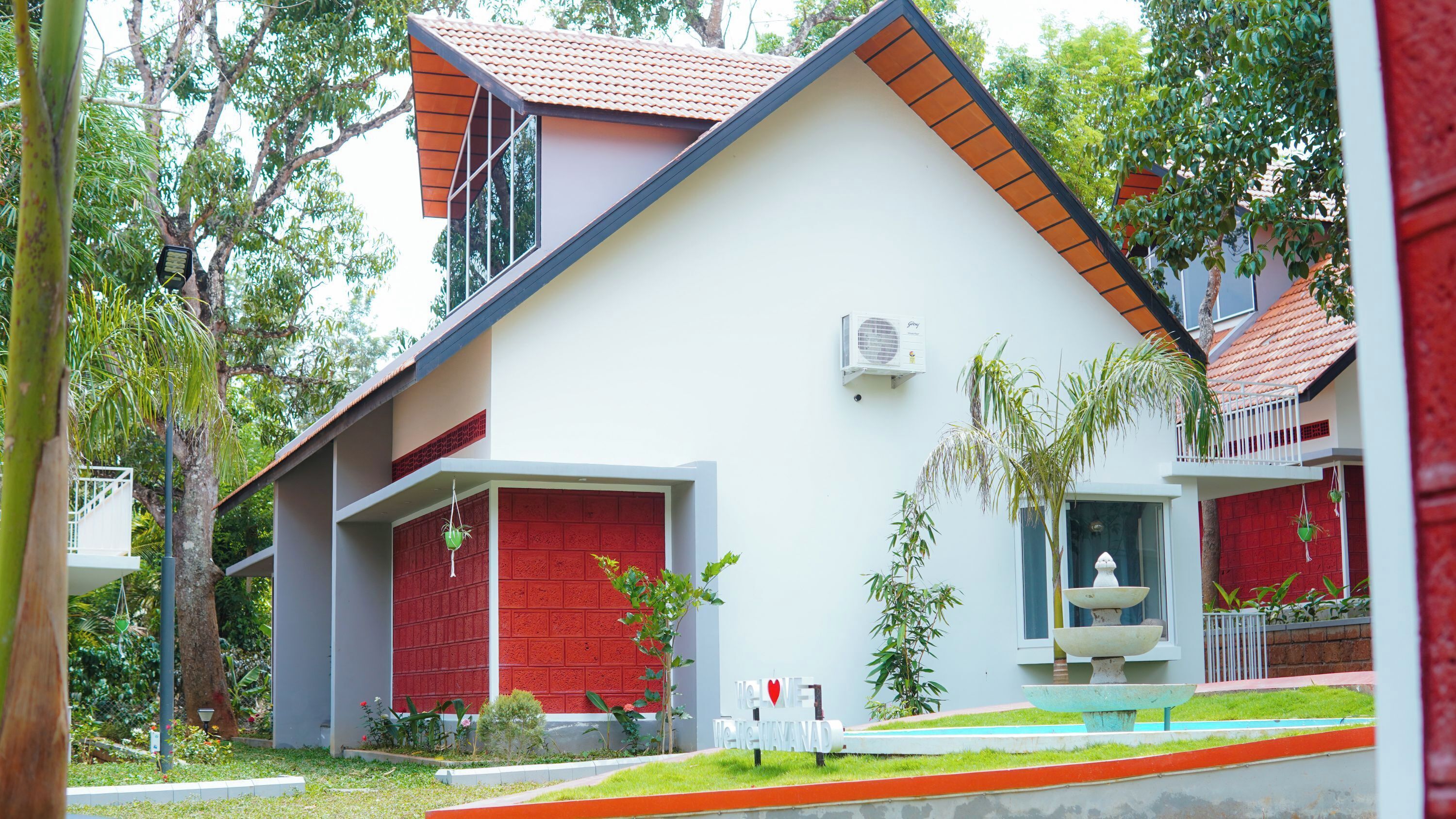 A modern house with a red door, a white exterior, and a small garden with a fountain.